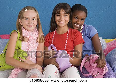 Stock Image - Portrait of three girls (10-11) with purses on sofa. Fotosearch