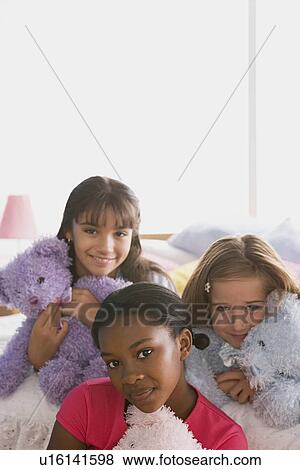 Stock Photo - Portrait of three girls (10-11) with puppets in bed. Fotosearch