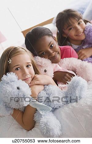 Stock Image - Portrait of three smiling girls (10-11) with puppets in bed. Fotosearch