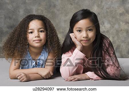 Stock Photo - Portrait of two girls (8-9) looking at camera, studio shot. Fotosearch