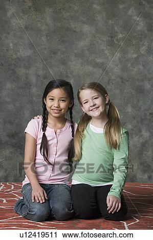 Stock Image - Portrait of two girls (8-9) posing together, studio shot. Fotosearch