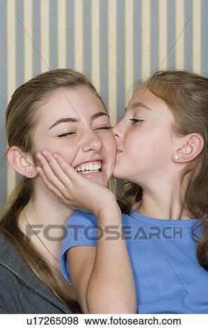 Stock Photo - Portrait of two sisters (14-15, 8-9) kissing . Fotosearch