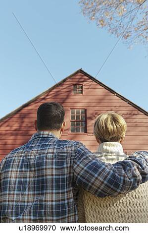 Stock Image - Rear view of couple facing cottage house. Fotosearch