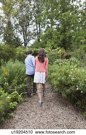 Stock Image - Rear view of couple walking through garden. Fotosearch