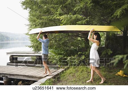 Stock Image - Roaring Brook Lake, Couple carrying boat by lake. Fotosearch