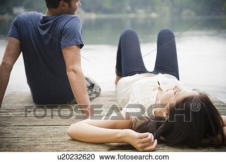 Stock Image - Roaring Brook Lake, Couple lying on pier. Fotosearch