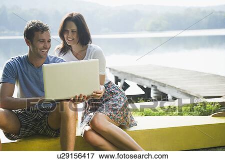 Stock Photo - Roaring Brook Lake, Couple using laptop by lake. Fotosearch
