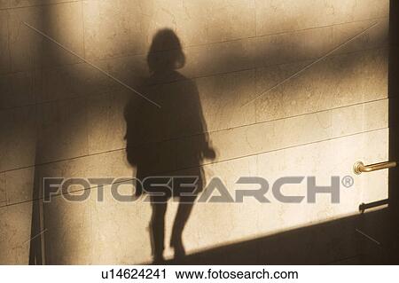 Stock Image - Shadow of single male pedestrian on sunlit wall. Fotosearch