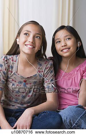Stock Photograph - Sisters (8-9, 10-11) listening together to music on headphones. Fotosearch