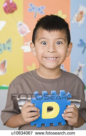 Stock Photo - Smiling boy (6-7) holding letter D. Fotosearch