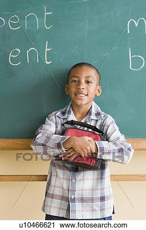 Smiling boy (6-7) holding lunch box against blackboard View Large Photo Image Stock Image - Smiling boy (6-7) holding lunch box against blackboard. Fotosearch