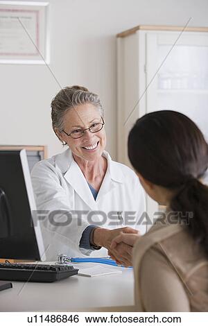 Smiling female doctor shaking hand with patient in her office View Large Photo Image Stock Photograph - Smiling female doctor shaking hand with patient in her office. Fotosearch