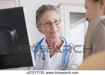 Stock Image - Smiling female doctor talking to patient in her office. Fotosearch