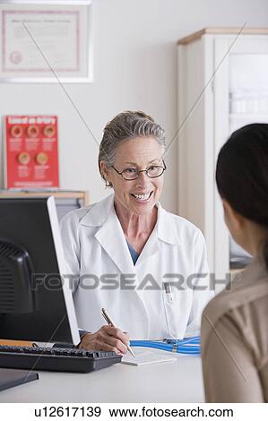 Stock Photo - Smiling female doctor talking to patient in her office. Fotosearch