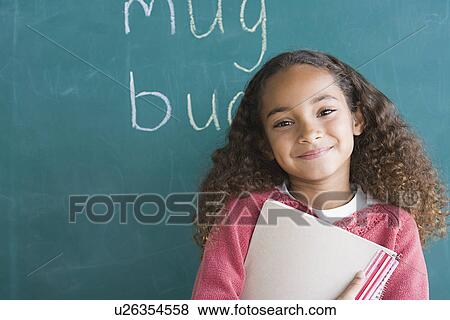 Stock Photo - Smiling girl (6-7) against blackboard. Fotosearch