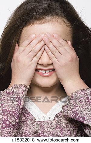 Stock Photo - Smiling girl (8-9) covering her eyes, studio shot. Fotosearch