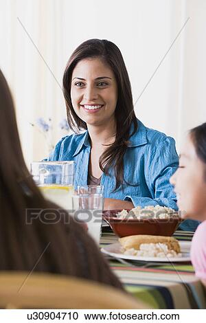 Stock Image - Smiling woman dining with daughters (8-9, 10-11). Fotosearch