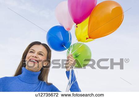Stock Image - Smiling woman holding balloons. Fotosearch