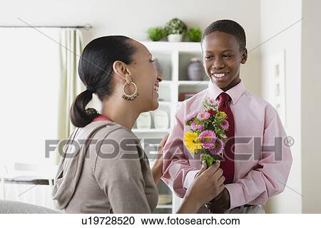 Stock Image - Son (12-13) giving flowers to Mother. Fotosearch