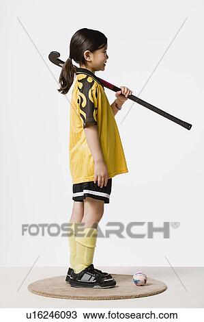 Stock Image - Studio portrait of girl (8-9) wearing sports clothes and holding hockey stick. Fotosearch