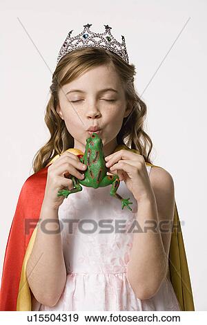 Stock Photo - Studio portrait of girl (8-9) wearing princess costume and kissing toy frog. Fotosearch