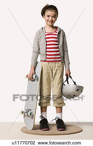 Stock Image - Studio portrait of girl (8-9) with skateboard. Fotosearch