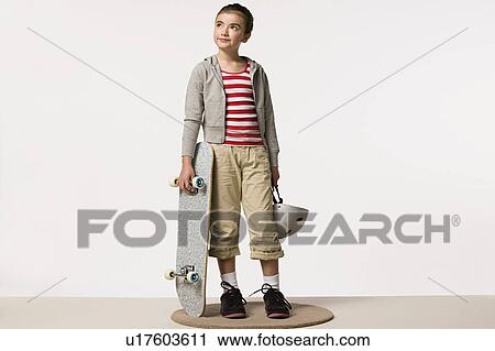 Stock Image - Studio portrait of girl (8-9) with skateboard. Fotosearch
