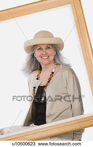 Stock Image - Studio portrait of mature woman behind picture frame. Fotosearch
