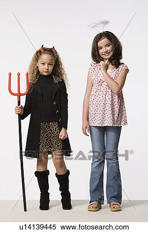 Stock Photography - Studio portrait of two girls (8-9) wearing Halloween costumes with trident and halo. Fotosearch