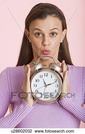 Studio shot of woman holding alarm clock View Large Photo Image Stock Image - Studio shot of woman holding alarm clock. Fotosearch