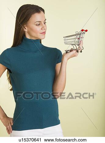 Stock Image - Studio shot of woman holding small shopping cart. Fotosearch