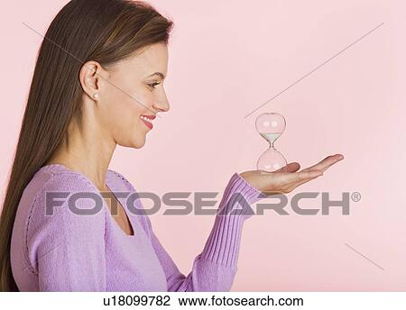 Stock Image - Studio shot of woman holding small hourglass. Fotosearch
