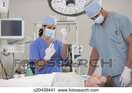 Stock Image - Surgeons preparing patient for surgery. Fotosearch