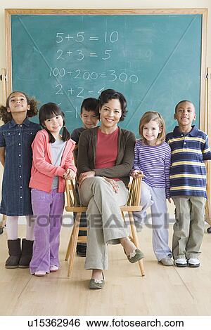 Stock Photograph - Teacher and children (6-7) posing in classroom. Fotosearch