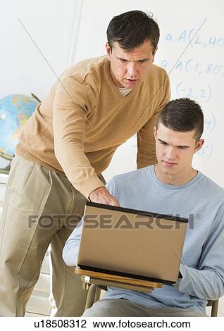 Stock Image - Teacher helping teenage (16-17) student . Fotosearch