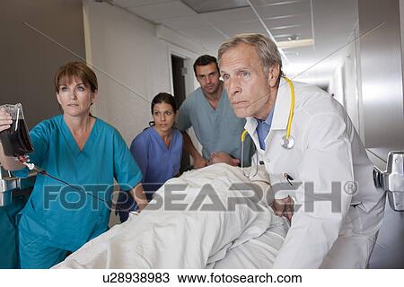 Stock Image - Team of doctors wheeling in patient. Fotosearch
