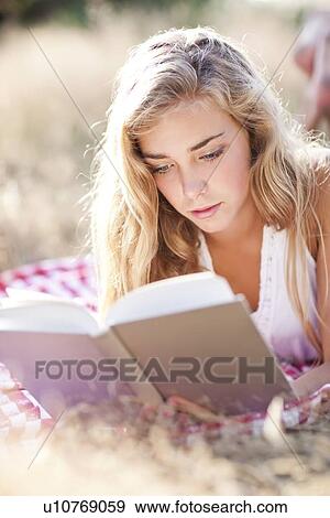 Stock Photo - Teenage girl (16-17) reading book outdoors. Fotosearch
