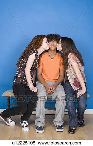 Stock Photography - Teenage girls (16-17) kissing teenage boy (14-15). Fotosearch