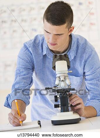 Stock Image - Teenage student (16-17) with microscope doing notes. Fotosearch