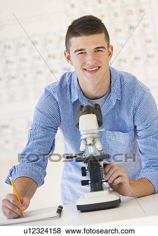 Stock Photo - Teenage student (16-17) with microscope doing notes. Fotosearch