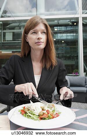 Stock Image - The Netherlands, Amsterdam, Portrait of businesswoman eating salad in cafe. Fotosearch