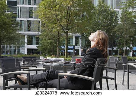 Stock Photo - The Netherlands, Amsterdam, Businesswoman relaxing on chairs on sidewalk. Fotosearch