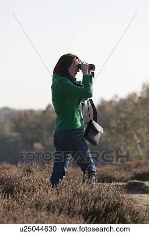 Stock Image - The Netherlands, Veluwezoom, Posbank, Woman in countryside looking through binoculars. Fotosearch