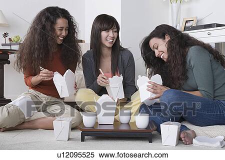 Stock Photography - Three female friends eating take out food at home. Fotosearch