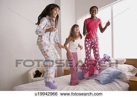Stock Photograph - Three girls (10-11) jumping on bed at slumber party. Fotosearch