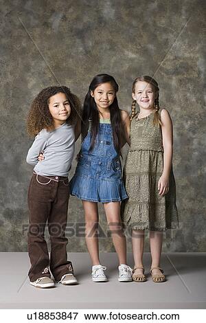 Stock Photo - Three smiling girls (8-9) standing together, studio shot. Fotosearch