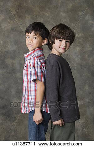Stock Image - Two boys (6-7, 8-9) posing back to back, studio shot. Fotosearch