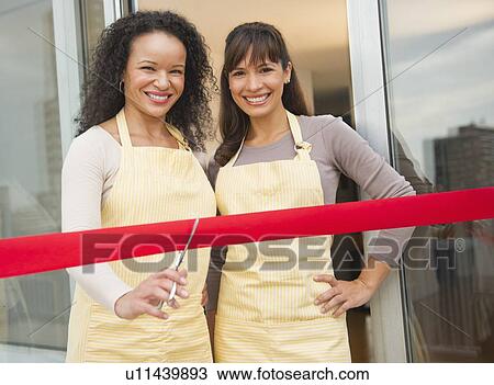 Stock Image - Two female business owners cutting red ribbon. Fotosearch
