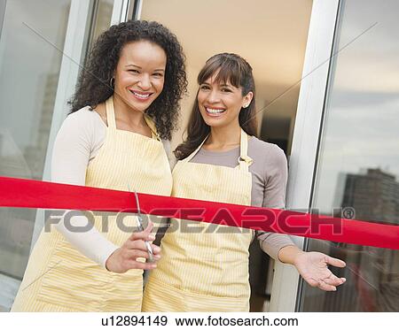 Stock Photo - Two female business owners cutting red ribbon. Fotosearch