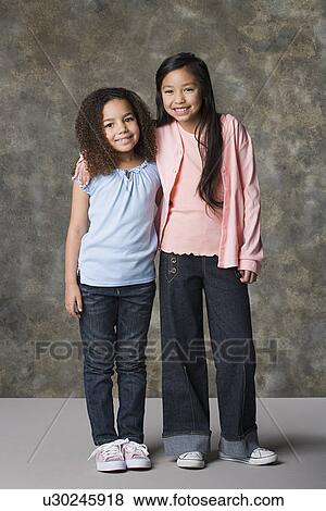Stock Photo - Two smiling girls (8-9) standing together, studio shot. Fotosearch